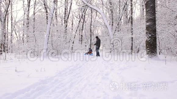 年轻的爸爸在冬天的小巷里把儿子推到雪橇上。