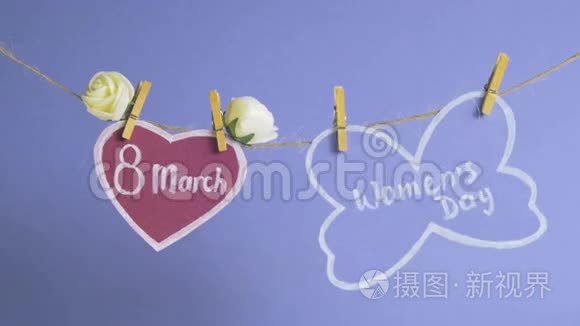 妇女节`快乐.. 妇女节`纸上，挂在一根绳子上，靠近粉红色的纸心，蓝色的背景上有花。