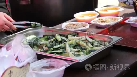 柜台上的女人用塑料盘子分发食物，里面有汤和粥。 附近有黄瓜