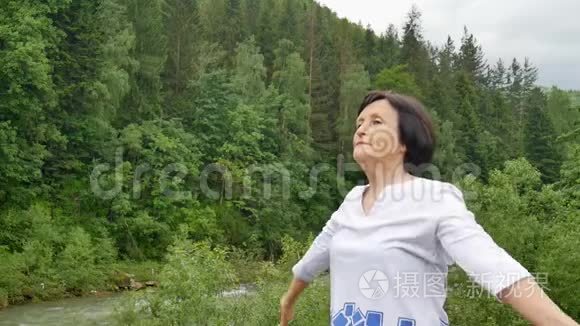 一位年长的女士在森林和山脉的外面为上臂做伸展运动