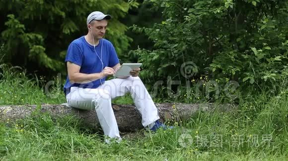 男人坐在原木上，拿着小玩意，耳机，听音乐，微笑