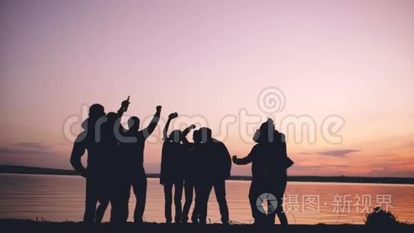 团体青年舞蹈家在日落时在海滩上举行派对