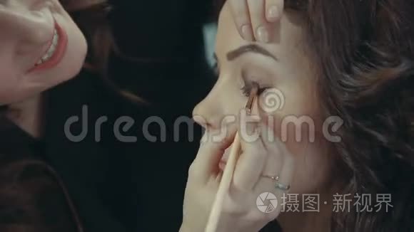 一位年轻的女造型师在一个深色模特的眼皮上画着一个深色的眼影。