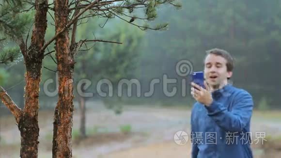 一个人在森林里的一棵树附近通过电话打视频电话。 清晨