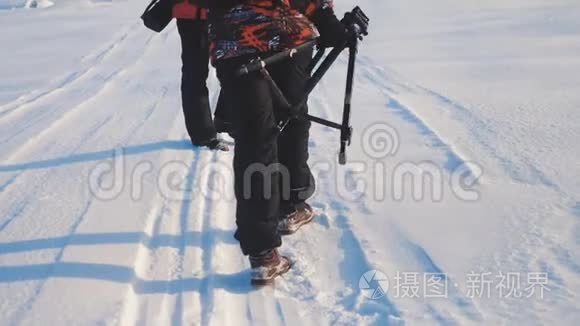 团队合作。 男游客摄影师在冬天乘三脚架爬山顶山顶岩峰群去雪