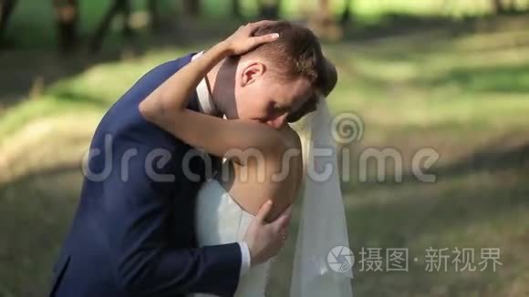新娘和新郎拥抱，亲吻和微笑在他们的婚礼当天，在公园。