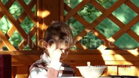 男孩在户外的露台上吃饭，困倦的男孩，害羞的相机