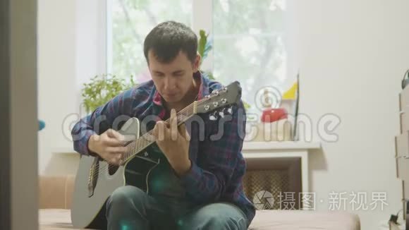 吉他手演奏和唱歌。 男子演奏声吉他慢动作视频。 在房间里坐在沙发上