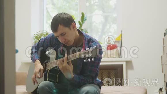 吉他手演奏和唱歌。 男子演奏声吉他慢动作视频。 在房间里坐在沙发上。 男人和男人