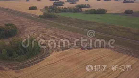 空中：在耕地上向无人机射击。一辆红色拖拉机在秋天开垦田地