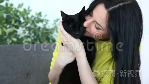 对宠物的爱。 美丽的黑发女孩带着一只黑猫在家里的沙发上客厅里放松。