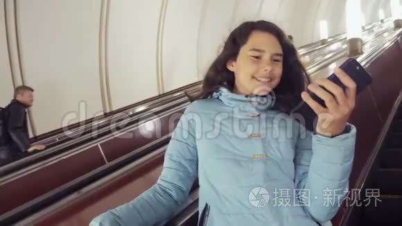 十几岁的女孩在地下地铁乘坐自动扶梯，持有智能手机。 小女孩，黑发女儿