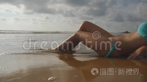 美丽的年轻女子躺在沙滩上的金色沙滩上，在暑假旅行中放松。 海洋海浪