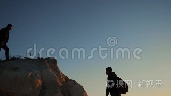 两个男子协同游客爬上一座山。 徒步旅行者徒步旅行冒险登山日落攀登