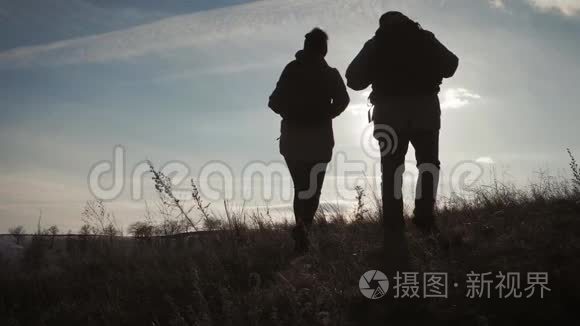两个徒步旅行者的剪影带背包，从山顶欣赏日落景色。 享受日落美景