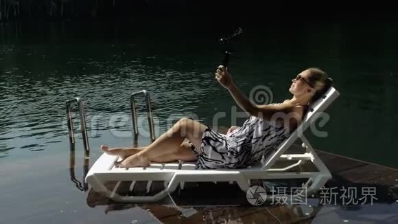 女性拍摄手持电影万向节稳定智能手机。 女孩躺在码头晒太阳自拍。 博客