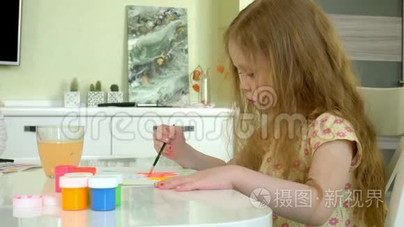 坐在桌旁的一个红发小姑娘画着颜料