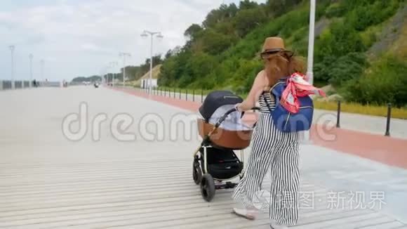 快乐的年轻母亲带着婴儿车在长廊散步。 家庭、母性和人的概念-有婴儿的幸福母亲