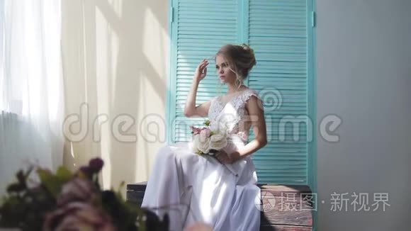 美丽的金发碧眼，穿着一件白色的新娘礼服，靠近一扇窗户，放着一束鲜花