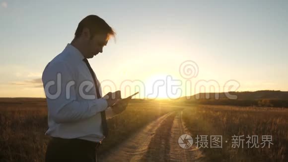 人类的双手正把手指压在平板电脑上。 男人检查电子邮件。 在公园日落时分工作的商人