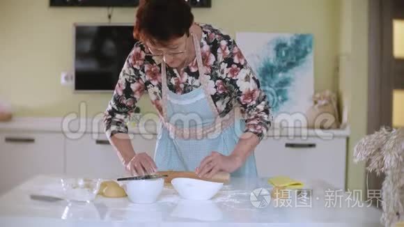 快乐的老妇人在家里厨房里擀饼干面团