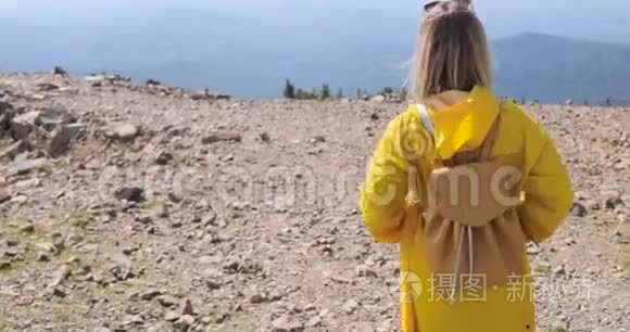 徒步旅行者背着背包在山顶徒步旅行。 穿着黄色雨衣的女孩在山顶上