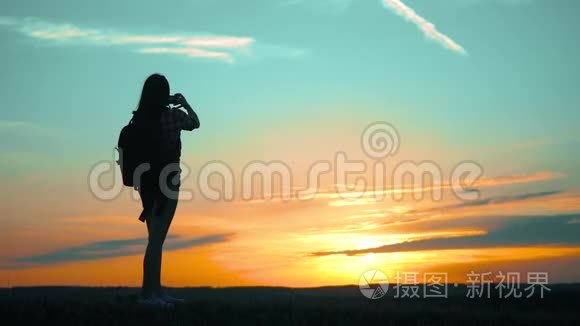 希普斯特的剪影女孩正在手机智能手机上拍摄美丽自然日落的视频