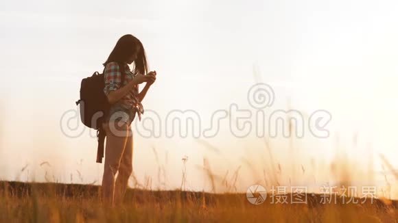 hipsterhiker剪影女孩正在手机智能手机上拍摄美丽自然日落的视频