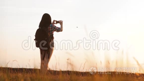 hipsterhiker剪影女孩正在手机智能手机上拍摄美丽自然日落的视频