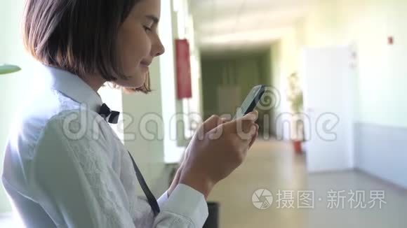 在学校概念上使用智能手机的女学生教育。 十几岁的小女孩，用智能手机站在窗口