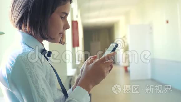 在学校概念上使用智能手机的女学生教育。 十几岁的小女孩，用智能手机站在窗口