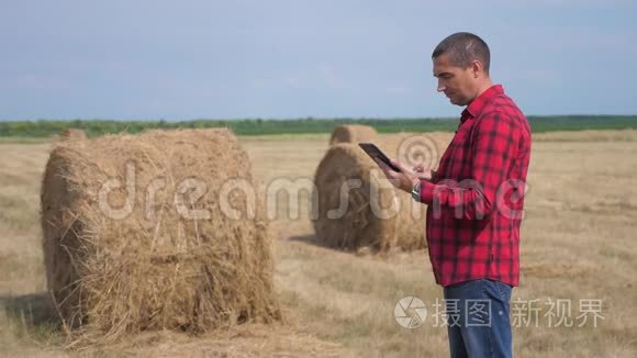 智慧生活方式农耕农业理念.. 一个工人农民在数字平板电脑上的田野里研究干草堆。 慢慢