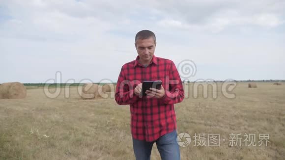 智慧农耕生活方式农业理念.. 一个农夫在数字平板电脑上的田野里研究干草堆。 慢动作