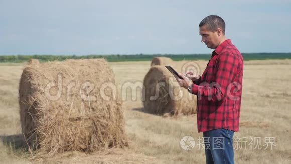 智慧农业理念.. 一名农民工人在数字平板电脑上的田野里研究干草堆的生活方式。 慢慢慢慢