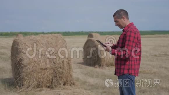 智慧农业理念.. 男子工人农民研究干草堆在田间生活方式的数字平板电脑。 慢慢