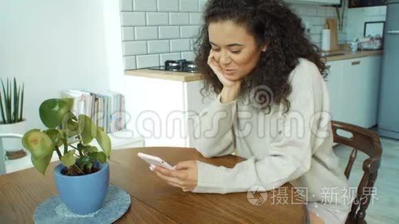 年轻的女人在厨房里用手机。