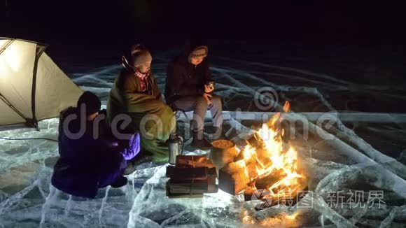 夜间有三个乘火的旅行者在冰上。 在冰上露营。 帐篷就在火旁边。 贝加尔湖。 就在附近