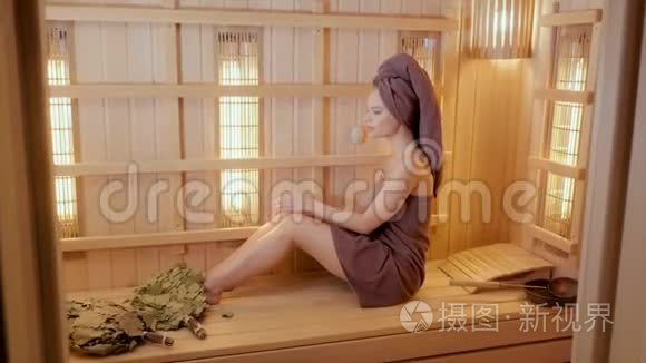 年轻女子穿着毛巾在桑拿浴室里放松。 新芬兰桑拿浴室内部，医疗用红外线面板