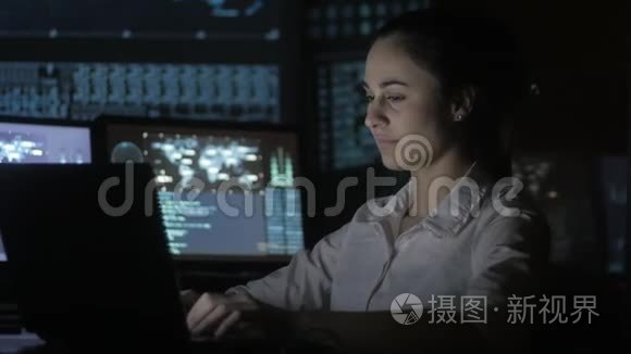 一幅年轻女性程序员在数据中心的一台电脑上工作的画像，里面装满了显示屏