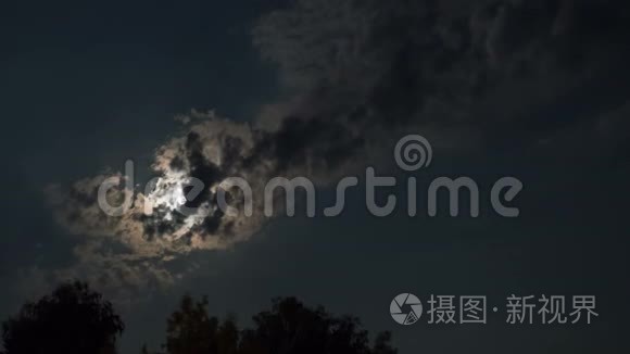 满月通过乌云和树木在夜空中移动。 时间流逝