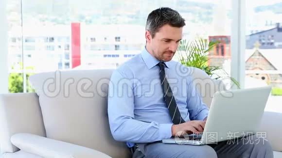 坐在沙发上的商人在打手提电脑视频