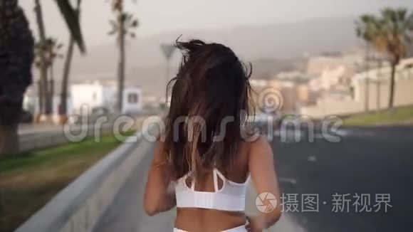 在柏油路边跑步的跑道妇女，穿着白色运动服沿着棕榈树林慢跑。 户外跑步的女人