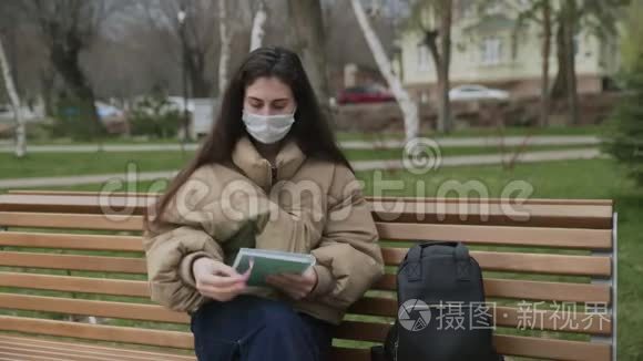 戴防护面具的年轻女子在城市公园的笔记本上写字。 大流行Covid-19冠状病毒保护。
