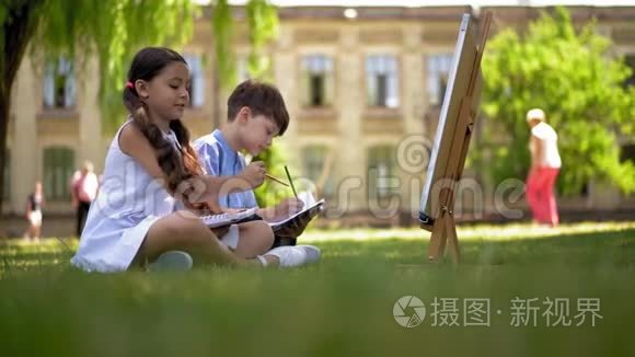 孩子们坐在绿草上画画。