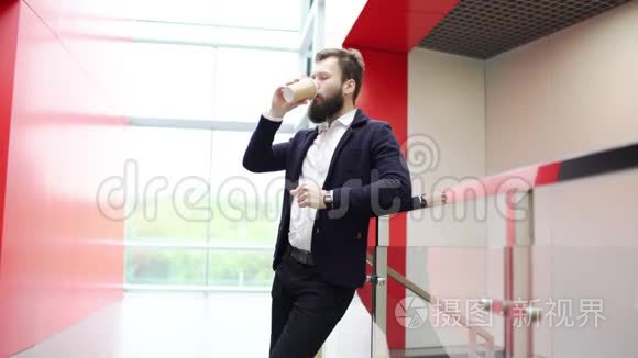 在现代办公大楼里，一个思想的人靠在篱笆上喝着咖啡，从前面看。 严重