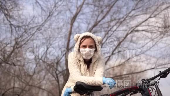 戴着医用口罩和手套的年轻女子站着，在乡下骑自行车。 女性保护自己