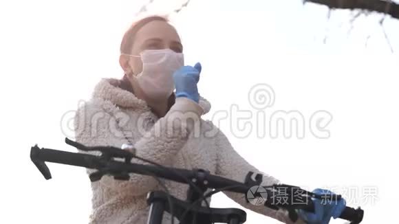 戴着医用口罩和手套的年轻女子咳嗽着，手握着农村自行车的舵。 保护妇女