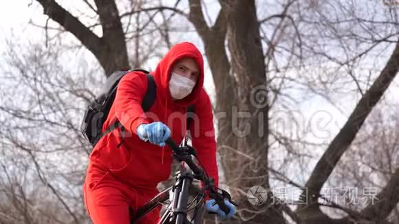 农村骑自行车的戴着医用口罩和手套的年轻人。 男性在散步时保护自己免受疾病的侵袭