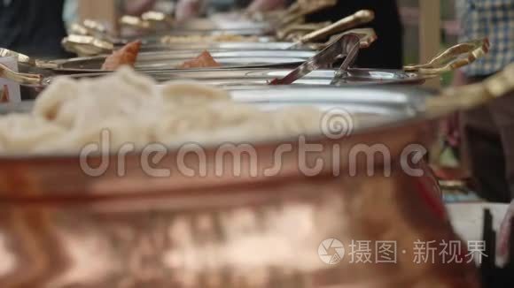 一排锡锅配有皮梅尼大米和其他亚洲食品。 背景是重点。 厨师的手在做食物。