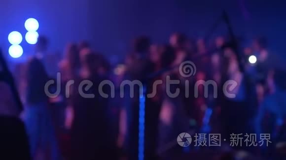 在音乐音乐会上，人们在舞池的夜总会里缓慢地随着电子音乐跳舞，模糊的轮廓